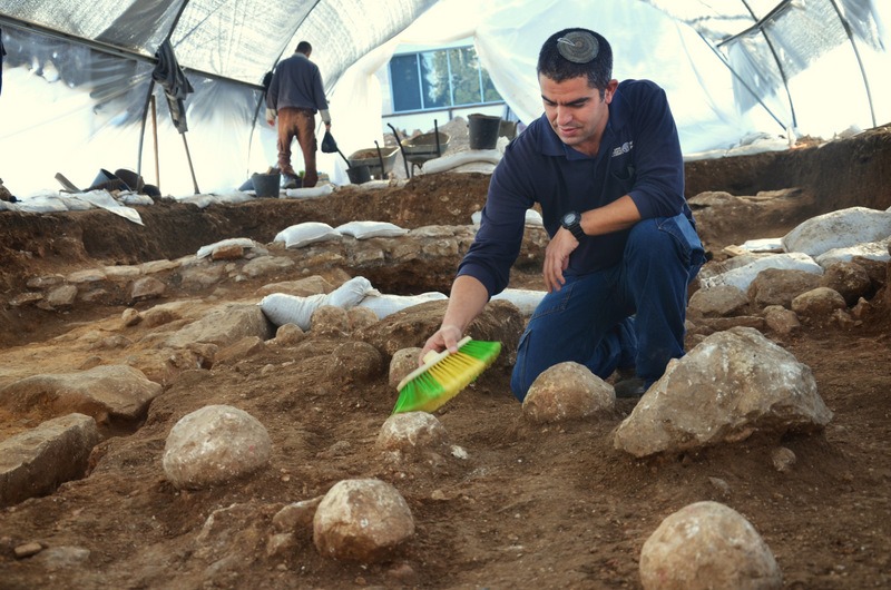 כפיר ארביב, מנהל החפירה מטעם רשות מהעתיקות, מנקה את אחת מאבני הקלע.